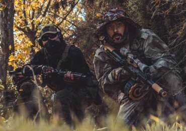 militaries holding weapons while hiding in the forest